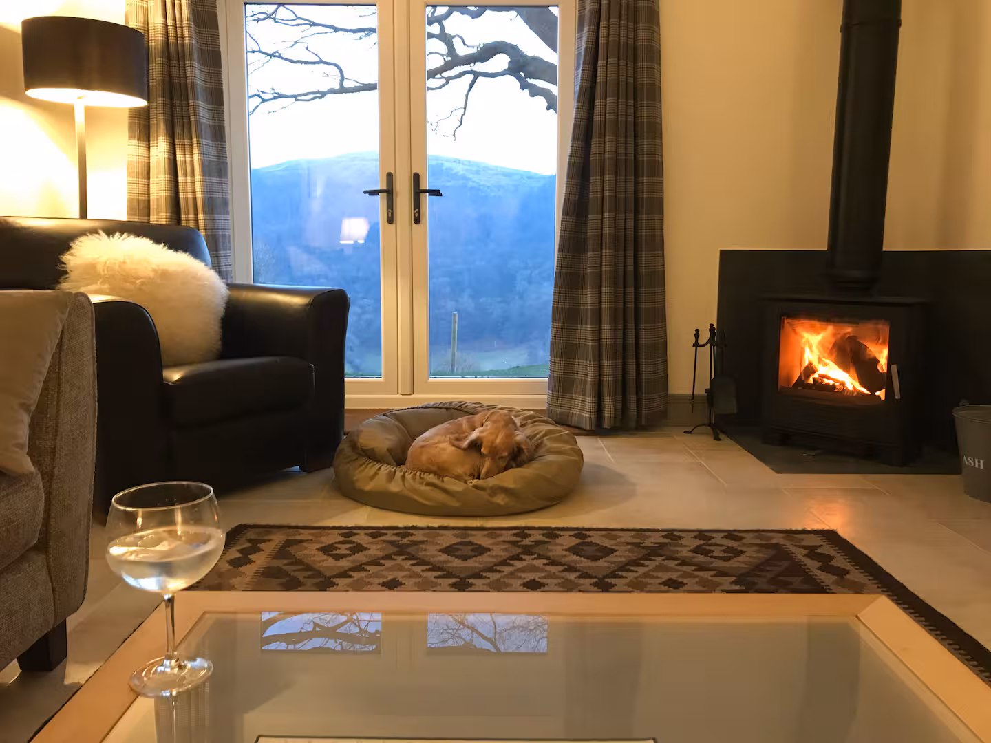 Log burner at The Barn, lit, beneath exposed oak trusses
