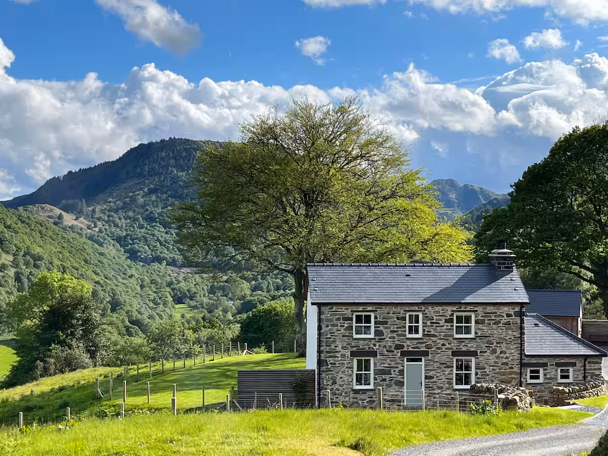 The Farmhouse — stone-built main house with sage green door, mature tree and Snowdonia mountains behind