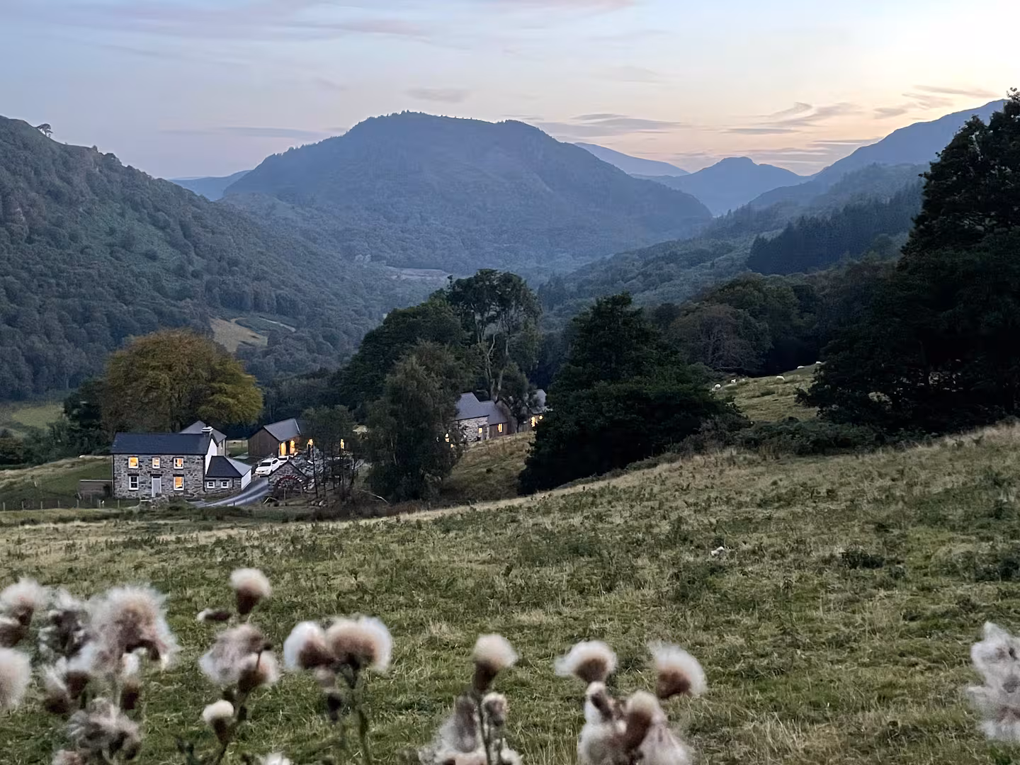 Gelli Newydd at dusk, three stone cottages with glowing windows set against the Snowdonia mountain valley